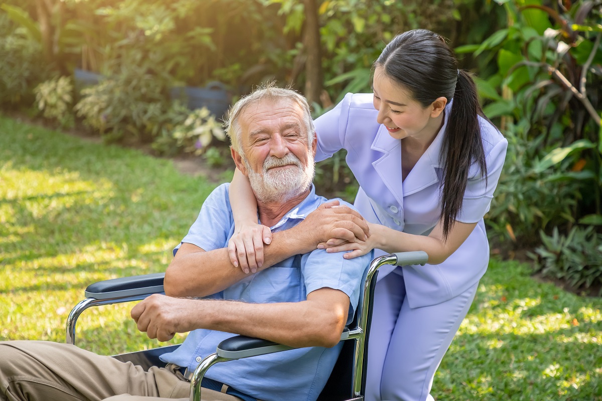 Happy nurse holding elderly man hand on wheelchair in garden at nursing home